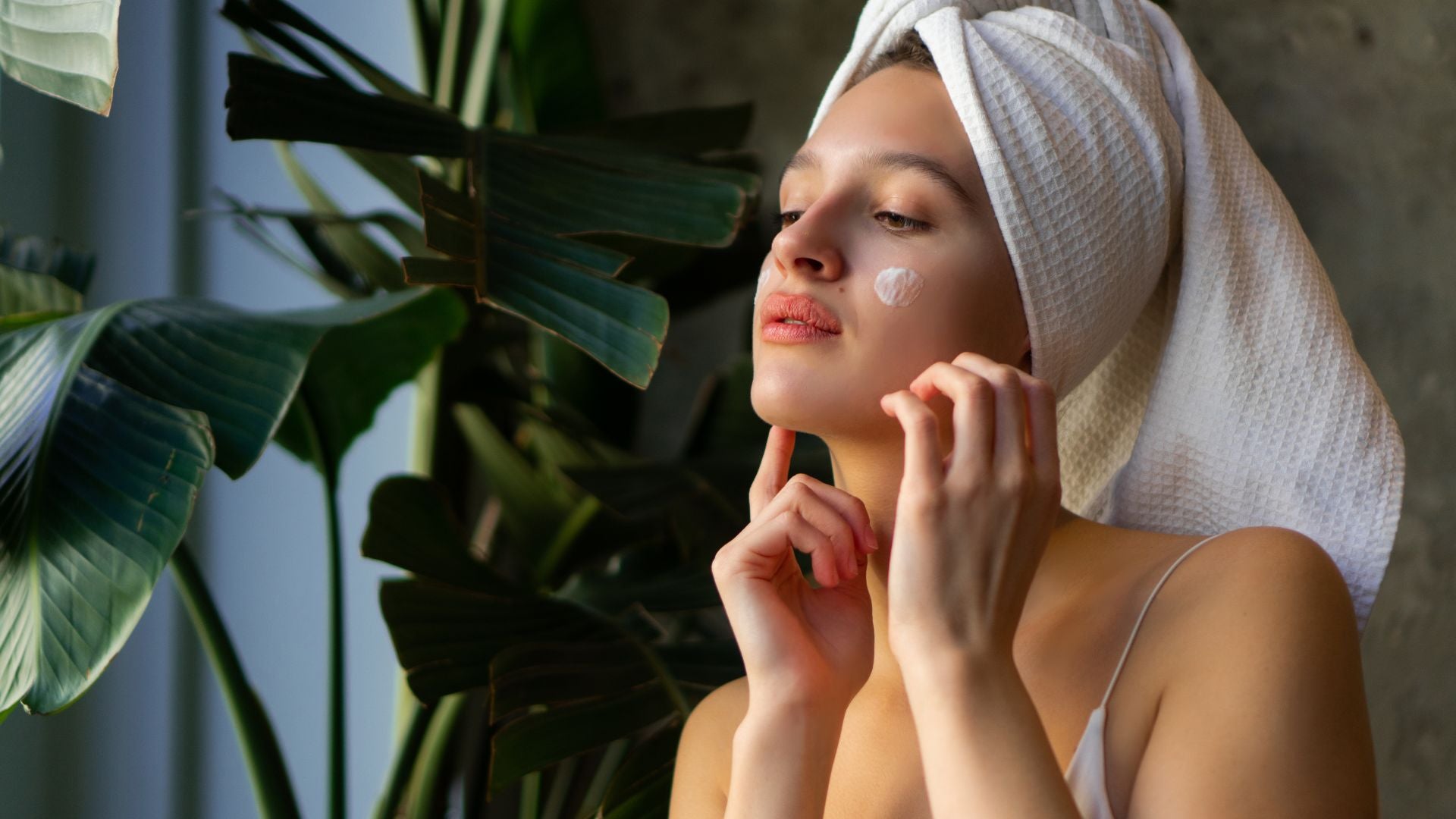 Woman with a towel turban applying a gentle BlushByEve moisturizer, embracing her clean beauty routine.
